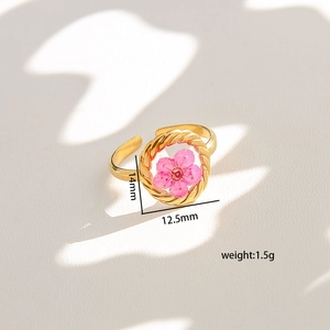 Detail view of gold stainless steel ring with dried pink flower in rope frame