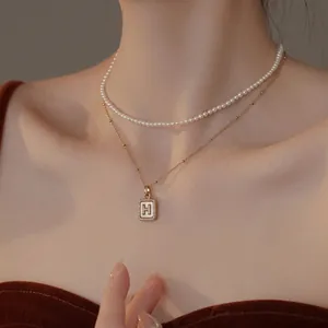 Close-up of a double-layered necklace featuring white pearls and a gold H-letter pendant