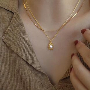 Gedetailleerde close-up van goudkleurige dubbele ketting met parelhanger en slangenketting