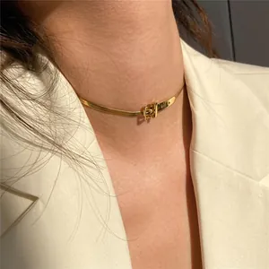 Detail view of a gold buckle choker necklace worn with a white professional blazer