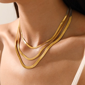 Close-up of layered gold herringbone snake bone necklaces on a model's neck.