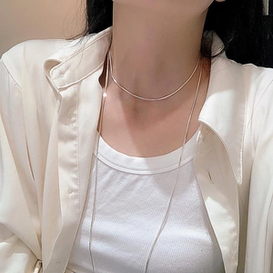 Detailed view of layered silver snake bone chains on a minimalist silk shirt background