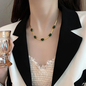 Detail van de gouden slangenketting met vijf smaragdgroene ovale stenen rond de nek