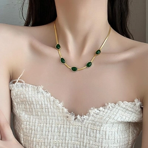 Detail van gouden slangenketting met vijf smaragdgroene druppelvormige edelstenen in vintage