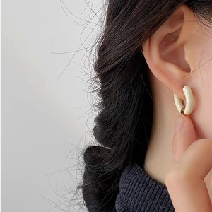 Detail of cream white enamel hoop earring with gold metal accent on female model