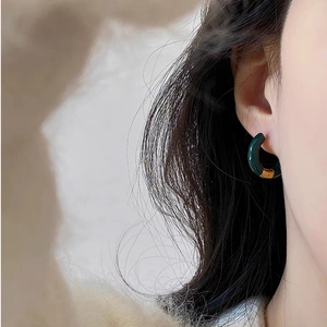 Close-up of a woman wearing a dark green enamel C-shaped hoop earring with gold metal accent