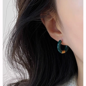 Close-up of a French retro C-shaped hoop earring in deep green enamel with gold accents