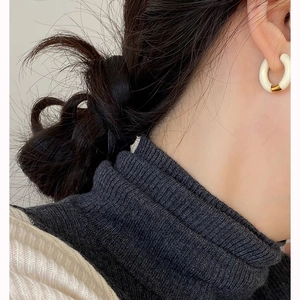 Close-up of a model wearing a minimalist ivory white resin C-shaped earring with gold link