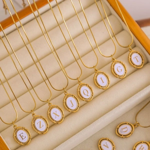 Gold plated stainless steel oval initial pendant necklaces on cream leather background