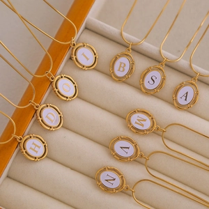 Detailed macro view of gold-plated snake chains with oval white enamel letter pendants