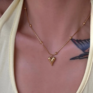 Minimalist gold heart pendant necklace with beaded chain worn by a female model