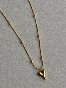 Macro detail of a minimalist gold heart pendant on a delicate beaded snake chain necklace