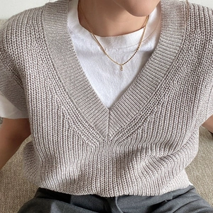 Dettaglio ravvicinato del gilet in maglia grigio chiaro con scollo a V e trama spessa