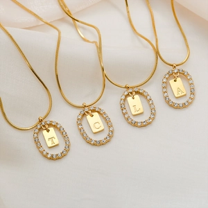 Detail of four gold stainless steel letter pendants with cubic zirconia on white silk