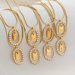Close-up of gold snake chain necklaces with crystal frames and engraved initial letter tags