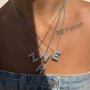 Macro detail of silver layered necklaces with Z, W, E, H letter pendants and pavé zircon