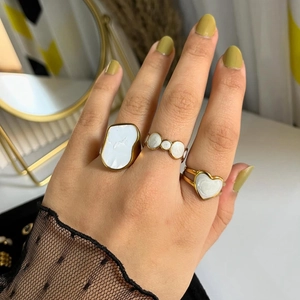 Détail de trois bagues dorées avec émail blanc en forme de cœur et géométrique