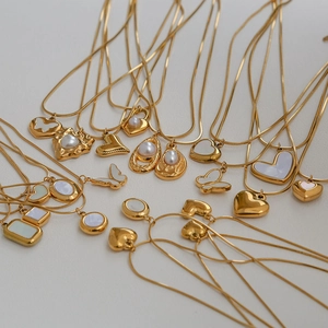 Collares de acero inoxidable dorado con colgantes de corazón y perla sobre fondo blanco