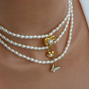 Dettaglio collana di perle a tre strati con ciondoli a cuore, lucchetto e farfalla dorati