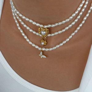 Dettaglio di una collana di perle a tre strati con lucchetto a cuore e farfalla dorata