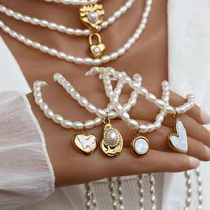 Dettaglio macro della collana in titanio dorato con cuori di perle e ciondoli a conchiglia