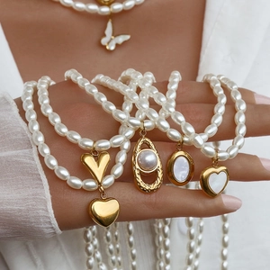 Dettaglio collana di perle placcata oro con ciondoli a cuore e conchiglia su modella