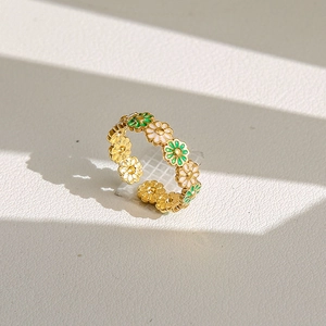 Détail de bagues marguerites dorées avec émail blanc et vert sous une ombre et lumière chic