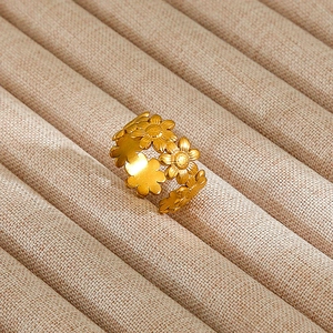 Detailed close-up of a gold floral stainless steel open ring on a beige linen display
