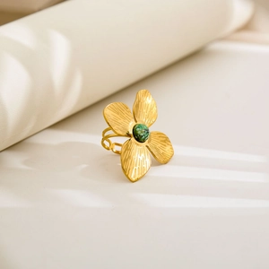 Close-up of golden floral ring featuring a green gemstone and brushed metal texture