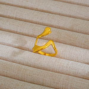 Dettaglio di un anello a forma di abbraccio dorato su un supporto in velluto beige