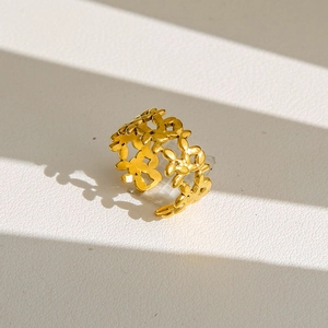 Gros plan d'une bague dorée en acier inoxydable avec motif floral ajouré et ombres douces