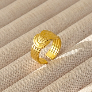 Dettaglio dell'anello geometrico dorato con texture a linee e design aperto regolabile