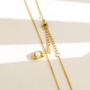 Dettaglio del ciondolo in oro 18K con perla e chiusura a moschettone su sfondo strutturato