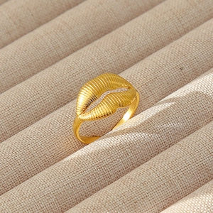 Dettaglio dell'anello placcato oro con trama verticale e forma a conchiglia su velluto beige