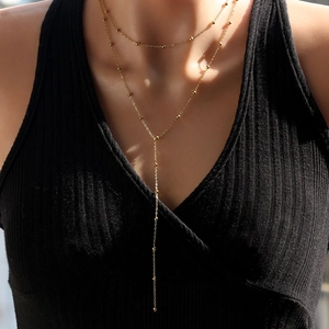Detail of layered gold Y-necklace with small beads worn over a black ribbed top