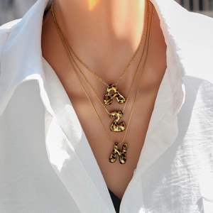 Primer plano de collares triple capa dorados con colgantes de letras en estampado animal