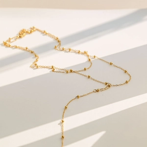 Close-up of a gold Y-shaped tassel necklace with tiny beads and elegant shadow patterns