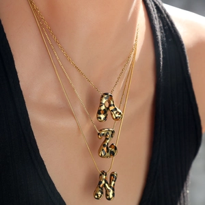 Primer plano de collares dorados con colgantes de letras gruesas con estampado de leopardo