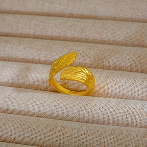 Dettaglio di un anello dorato con ali d'angelo e fascia regolabile su tessuto strutturato