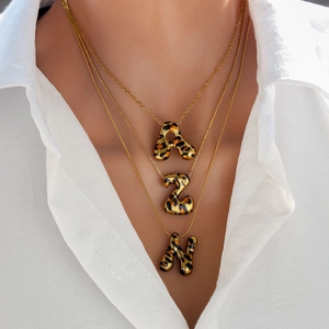 Detalle de collares dorados de tres capas con colgantes A, 2 y N con estampado de leopardo