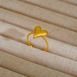 Dettaglio dell'anello a cuore dorato con fascia a corda su espositore in lino beige