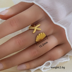 Anillo abierto de acero dorado con estrella de mar y concha usado en el dedo