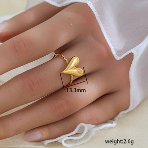 Detalle de anillo de corazón dorado con textura cepillada y banda trenzada en la mano