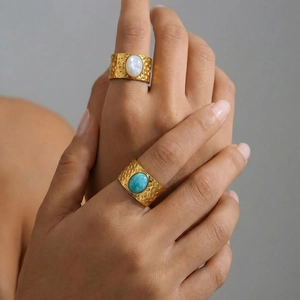 Golden hammered wide rings with oval white and turquoise stones worn by a model