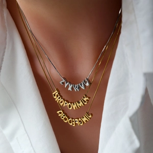 Collana a tre strati con pendenti a lettere in ottone oro e argento su camicia bianca