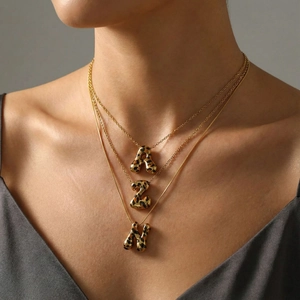 Conjunto de tres collares dorados con colgantes de letras de leopardo en una modelo