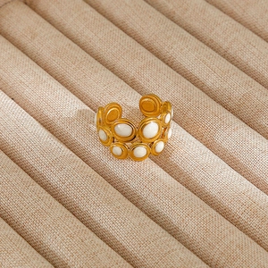 Detail of gold-plated double-row open ring with white stone inlays on beige jewelry stand