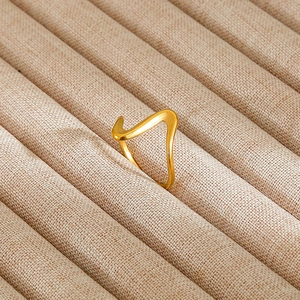 Detail of a wavy geometric gold ring with matte finish on a beige velvet jewelry tray