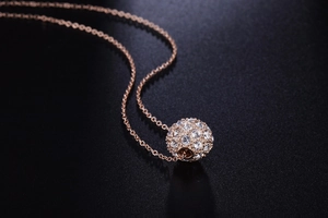 Gros plan du collier pendentif boule or rose avec pavé de cristaux sur fond noir texturé