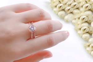 Detailweergave van een roségouden bruidsringset met zirkonia aan een hand met bloemen